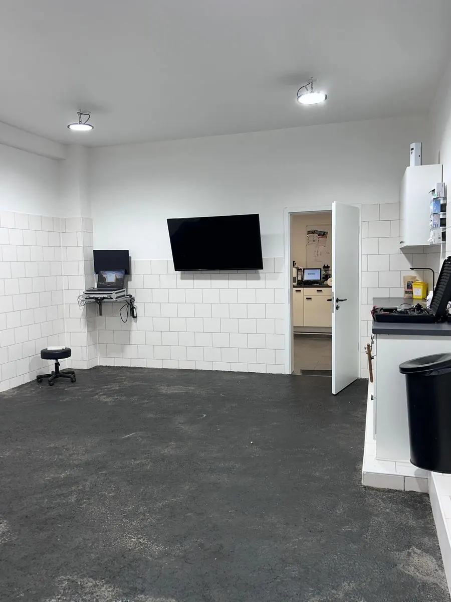 Heller Untersuchungsraum mit Monitor, durch die offene Tür ist das Labor zu sehen